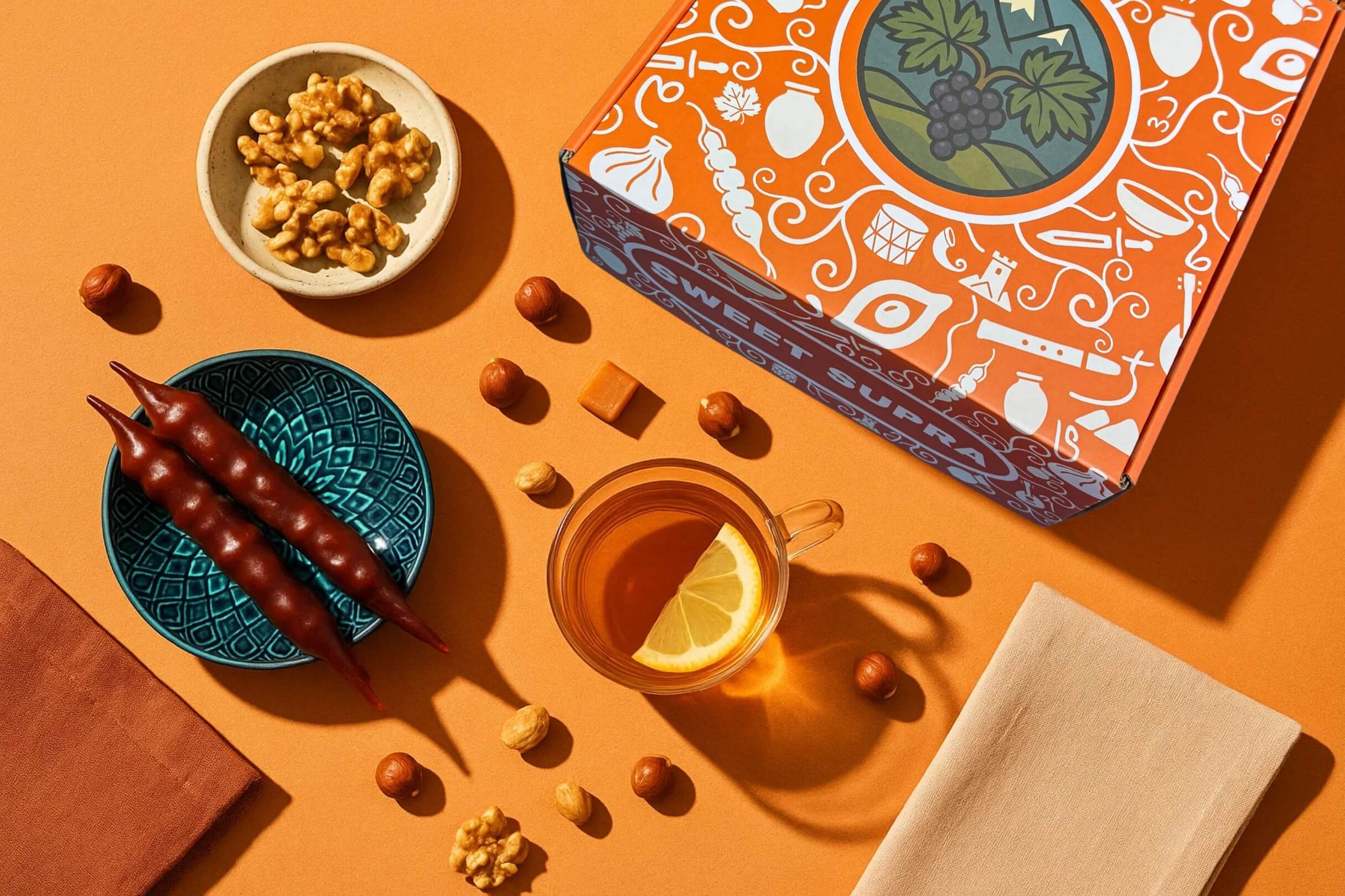 Sweet Supra Georgian snack gift box with churchkhela, nuts, and lemon tea on an orange table.
