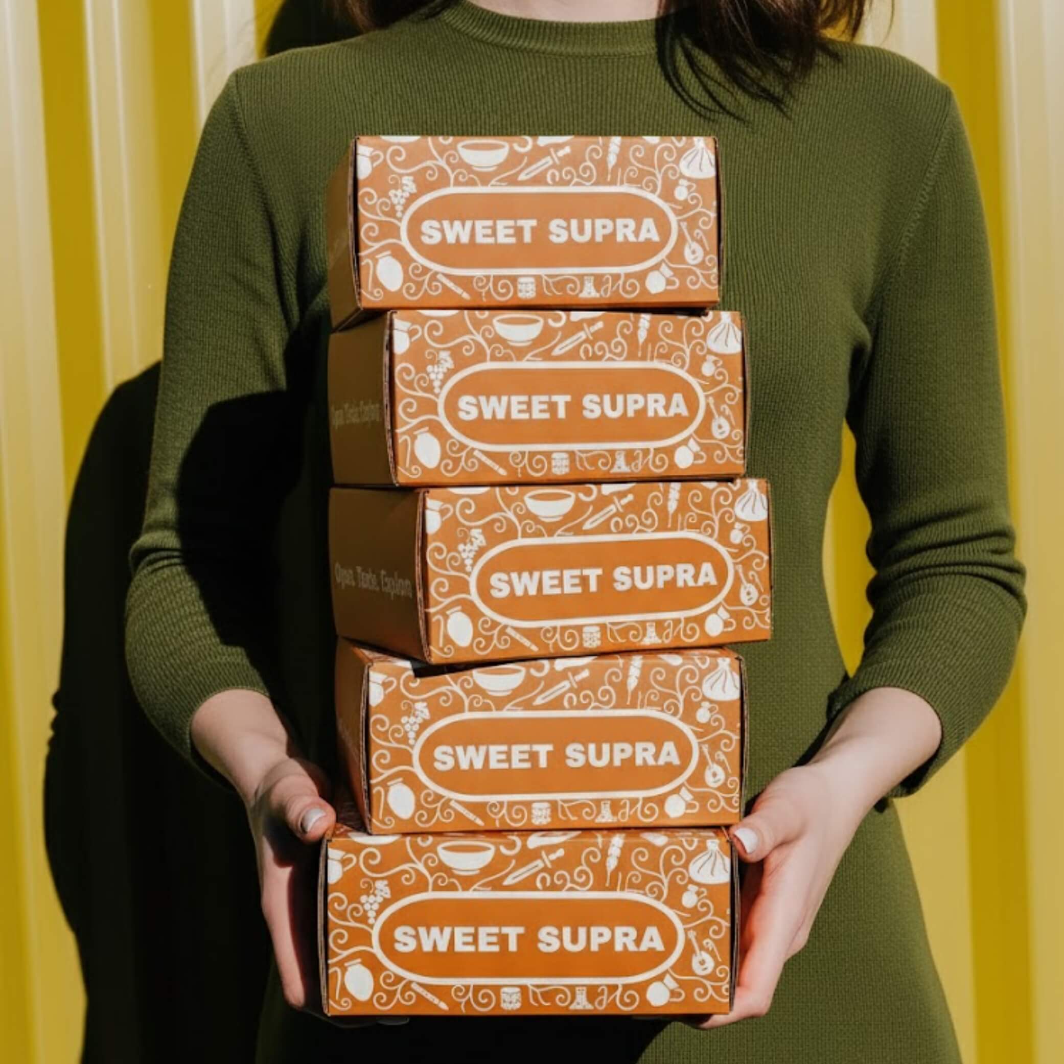 Person holding a stack of five Sweet Supra orange gift boxes.